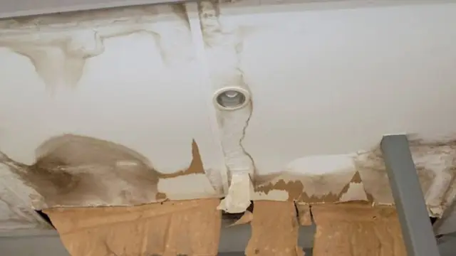 Water-stained ceiling with peeling paint and exposed material around a fixture